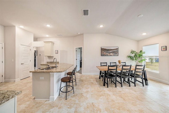 kitchen featuring light stone countertops, sink, white cabinetry, and vaulted ceiling