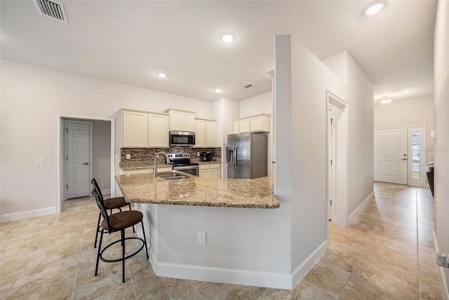 kitchen featuring a kitchen bar, light stone countertops, kitchen peninsula, backsplash, and stainless steel appliances