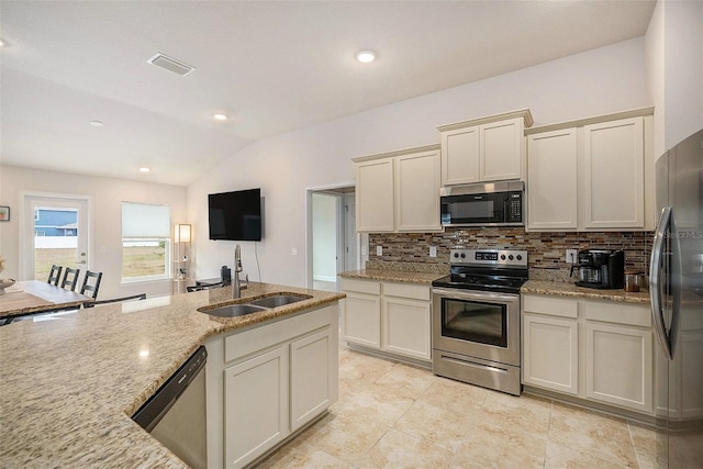 kitchen featuring appliances with stainless steel finishes, sink, cream cabinetry, light stone countertops, and lofted ceiling