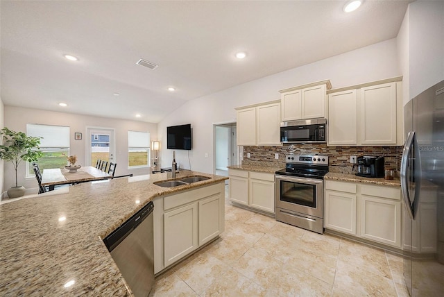 kitchen with cream cabinets, sink, stainless steel appliances, light stone counters, and lofted ceiling