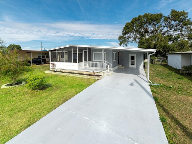 manufactured / mobile home with concrete driveway, an attached carport, a front yard, and a sunroom