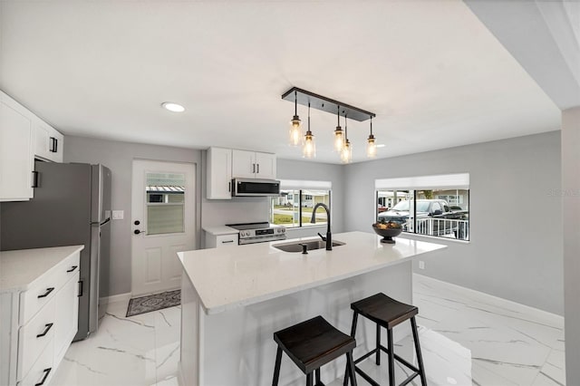 kitchen featuring pendant lighting, appliances with stainless steel finishes, sink, white cabinetry, and an island with sink