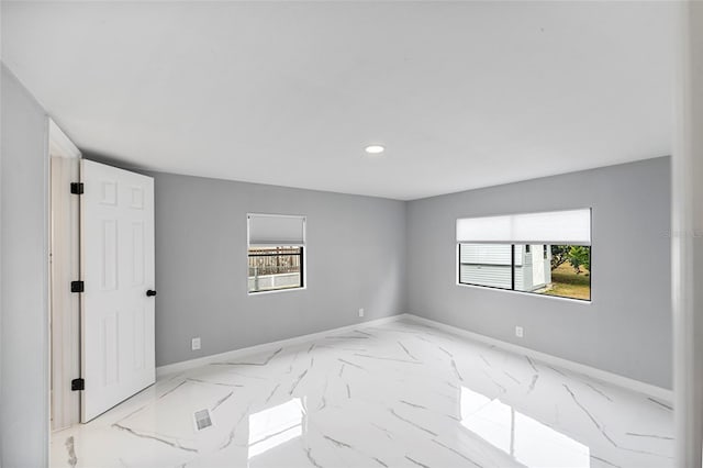 spare room featuring baseboards, marble finish floor, and a healthy amount of sunlight