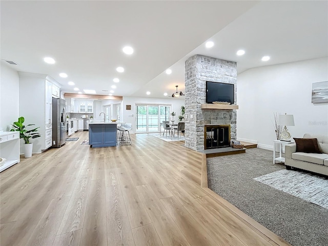 living room with sink, a stone fireplace, and light wood-type flooring