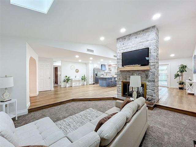 living room featuring a stone fireplace, vaulted ceiling, and hardwood / wood-style floors