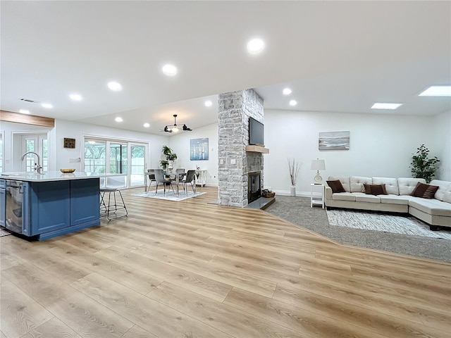 living room with sink, a fireplace, light hardwood / wood-style floors, and vaulted ceiling