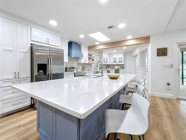 kitchen featuring appliances with stainless steel finishes, custom range hood, a breakfast bar area, and white cabinets