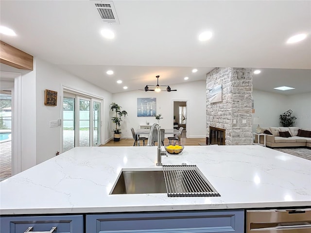 kitchen with blue cabinetry, sink, vaulted ceiling, a fireplace, and light stone countertops