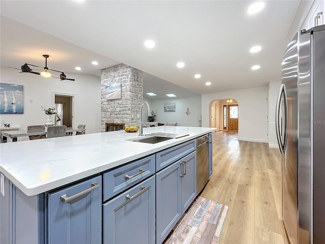 kitchen with sink, a center island with sink, appliances with stainless steel finishes, light stone countertops, and light hardwood / wood-style floors