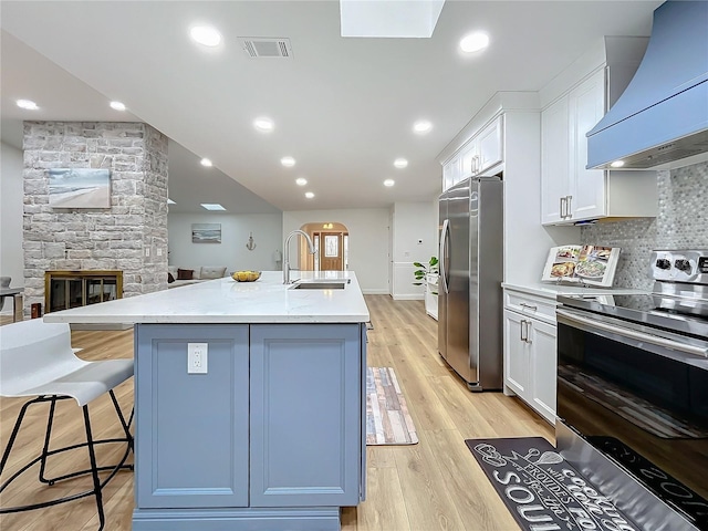 kitchen featuring premium range hood, sink, a center island with sink, appliances with stainless steel finishes, and white cabinets