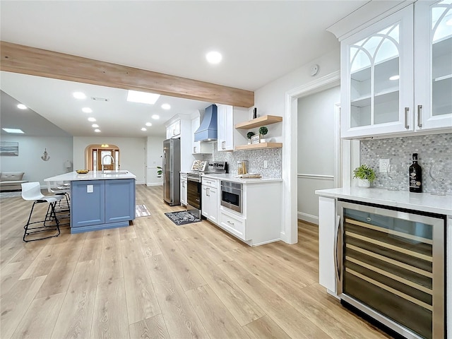 kitchen with a breakfast bar area, appliances with stainless steel finishes, white cabinets, beverage cooler, and wall chimney exhaust hood