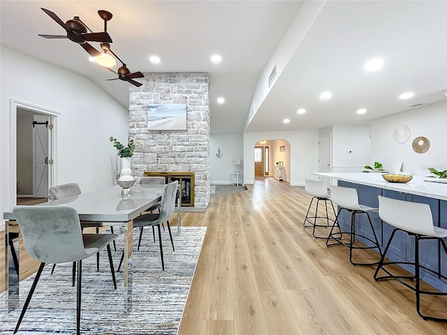 dining space featuring a fireplace, light hardwood / wood-style floors, ceiling fan, and vaulted ceiling