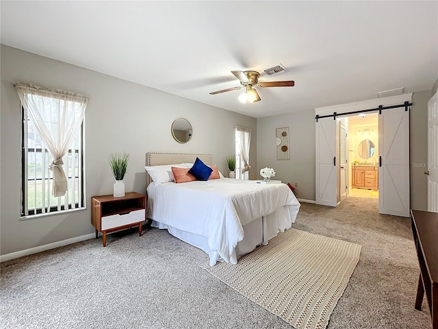 carpeted bedroom with a barn door, connected bathroom, and ceiling fan