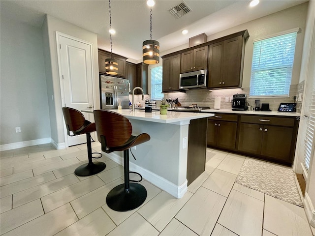 kitchen featuring pendant lighting, a breakfast bar, appliances with stainless steel finishes, a center island with sink, and decorative backsplash