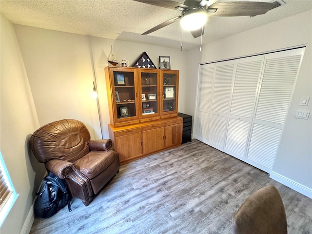 sitting room featuring light wood-type flooring, a textured ceiling, and ceiling fan