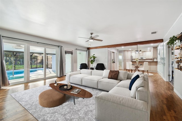 living room featuring baseboards, light wood-type flooring, visible vents, and a ceiling fan