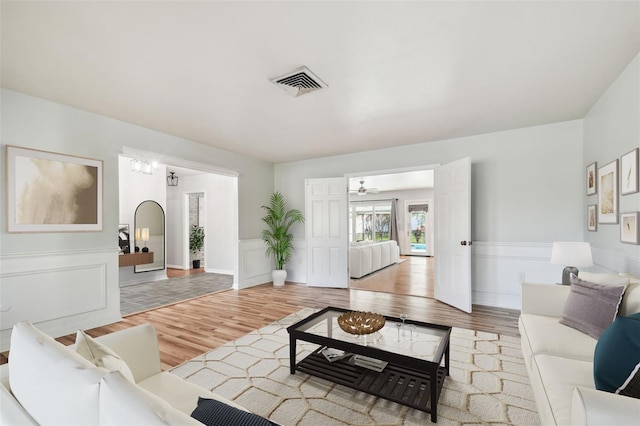 living room with wainscoting, wood finished floors, visible vents, and a decorative wall