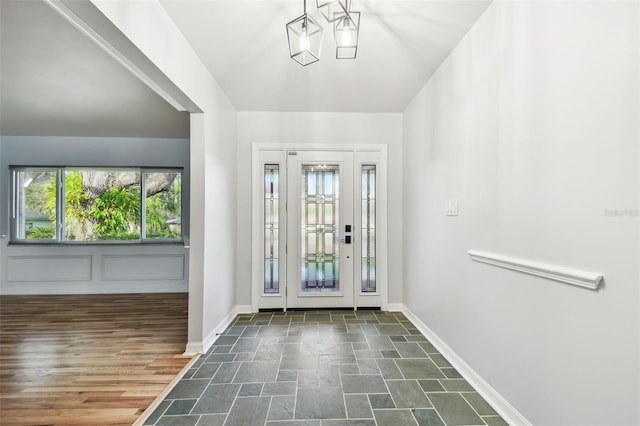 entrance foyer featuring a chandelier, baseboards, and stone tile floors