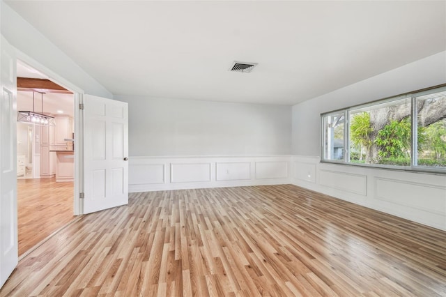 spare room featuring light wood-style flooring, wainscoting, and visible vents