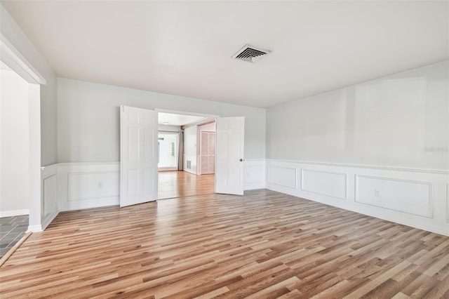 spare room with wainscoting, visible vents, and light wood finished floors