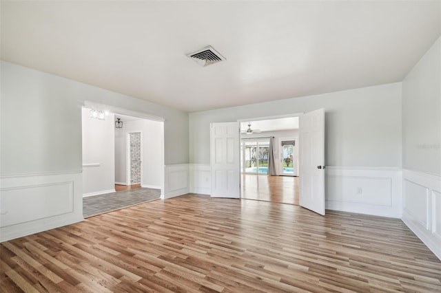 spare room featuring a wainscoted wall, light wood-style flooring, visible vents, and a decorative wall