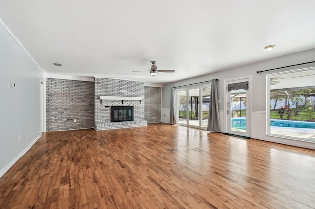 unfurnished living room featuring a brick fireplace, brick wall, visible vents, and hardwood / wood-style floors