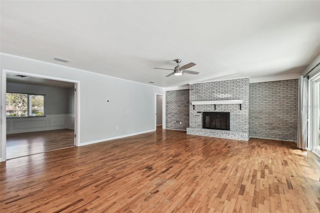 unfurnished living room with visible vents, a brick fireplace, ceiling fan, brick wall, and hardwood / wood-style flooring