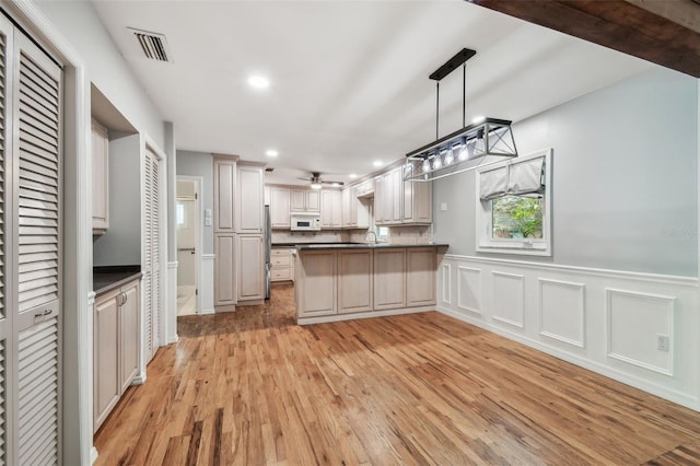 kitchen with white microwave, a peninsula, visible vents, freestanding refrigerator, and dark countertops