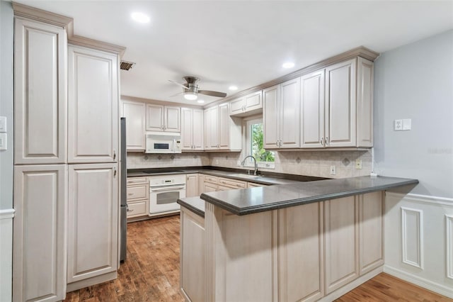 kitchen featuring a peninsula, white appliances, dark countertops, and wood finished floors