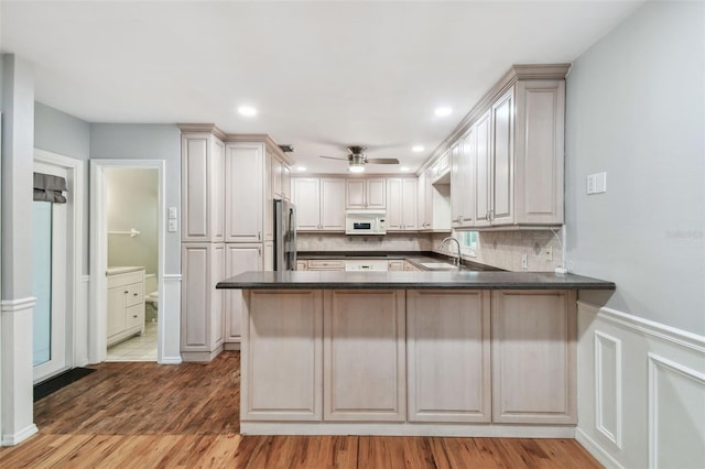 kitchen featuring white microwave, a peninsula, a sink, dark countertops, and stainless steel fridge