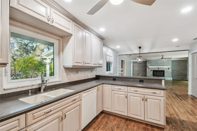 kitchen with dark countertops, white dishwasher, a peninsula, and a sink