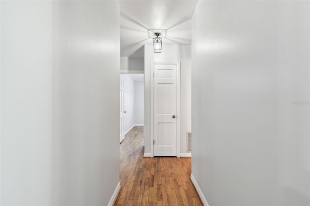 hall featuring light wood-type flooring, visible vents, and baseboards