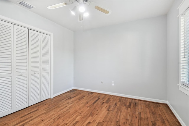 unfurnished bedroom featuring a closet, wood-type flooring, visible vents, a ceiling fan, and baseboards