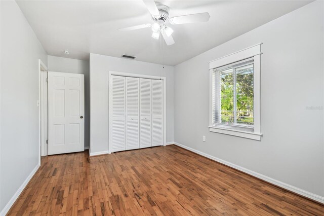 unfurnished bedroom with a closet, visible vents, a ceiling fan, wood finished floors, and baseboards