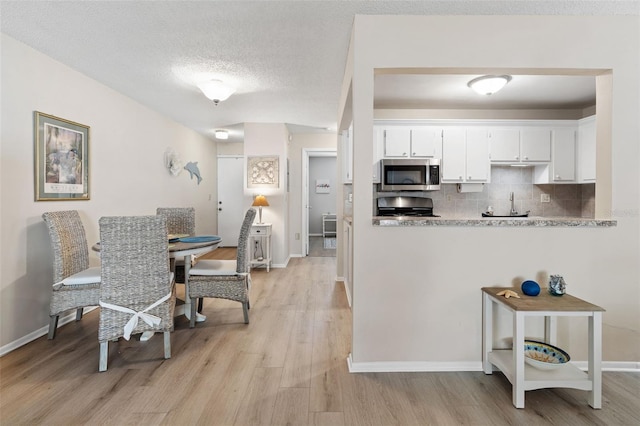 kitchen with range, white cabinetry, light stone countertops, decorative backsplash, and light wood-type flooring