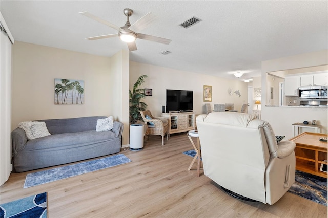 living room with ceiling fan, a textured ceiling, and light wood-type flooring