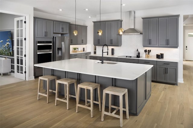 kitchen with sink, backsplash, a kitchen island with sink, wall chimney range hood, and stainless steel appliances