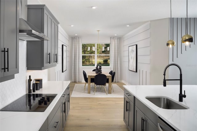 kitchen with light hardwood / wood-style floors, black electric cooktop, wall chimney range hood, decorative light fixtures, and sink