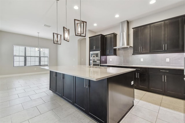 kitchen with hanging light fixtures, stainless steel microwave, a center island with sink, and wall chimney exhaust hood