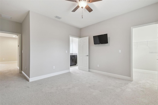 unfurnished bedroom featuring a walk in closet, ceiling fan, light colored carpet, and a closet