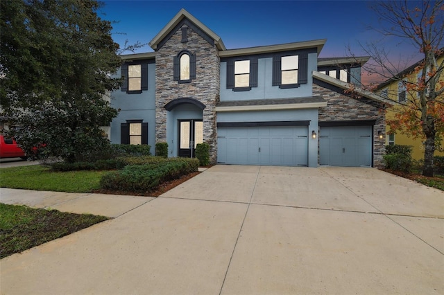 traditional-style house with stone siding, driveway, stucco siding, and an attached garage