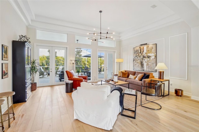 living room featuring crown molding, a chandelier, light hardwood / wood-style floors, and french doors