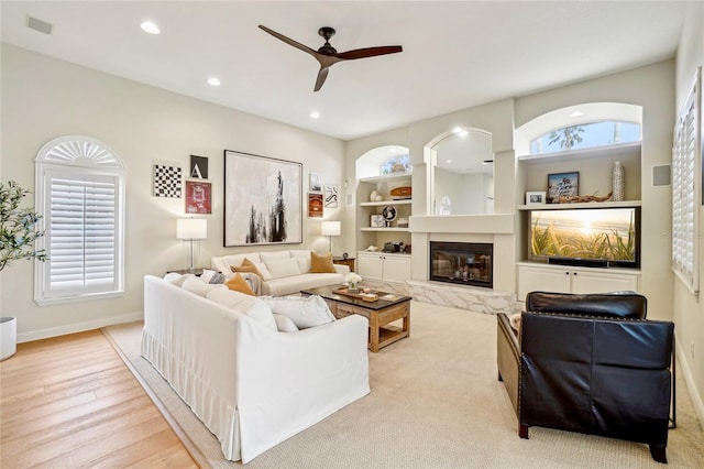 living room featuring ceiling fan, built in features, a fireplace, and light hardwood / wood-style flooring