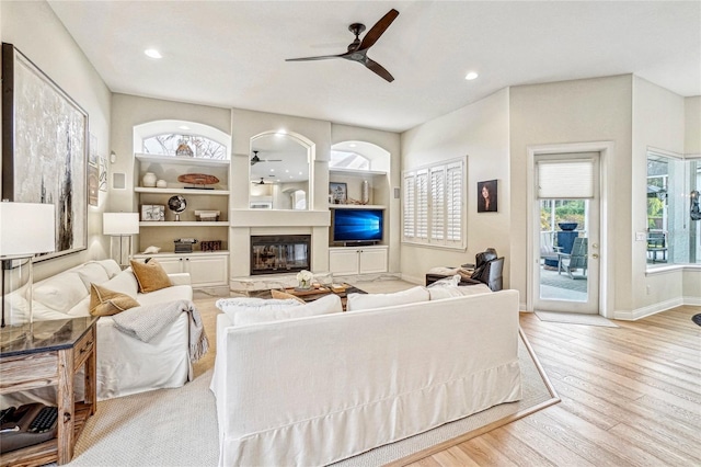 living room with built in shelves, ceiling fan, and light wood-type flooring