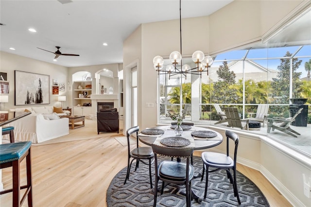 dining area with built in shelves, ceiling fan with notable chandelier, and light hardwood / wood-style flooring