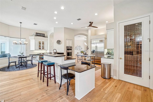 kitchen featuring a breakfast bar area, appliances with stainless steel finishes, hanging light fixtures, light hardwood / wood-style floors, and white cabinets