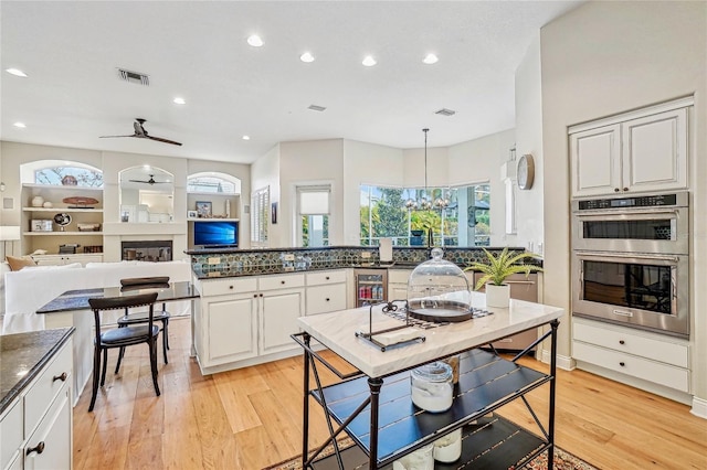 kitchen featuring light hardwood / wood-style flooring, built in features, white cabinetry, double oven, and decorative light fixtures