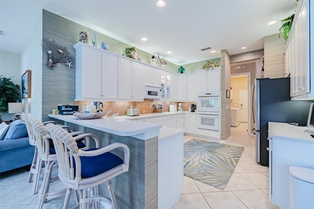 kitchen featuring white appliances, kitchen peninsula, a breakfast bar area, and white cabinets