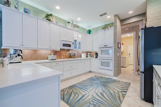 kitchen with light tile patterned flooring, tasteful backsplash, sink, white cabinets, and white appliances