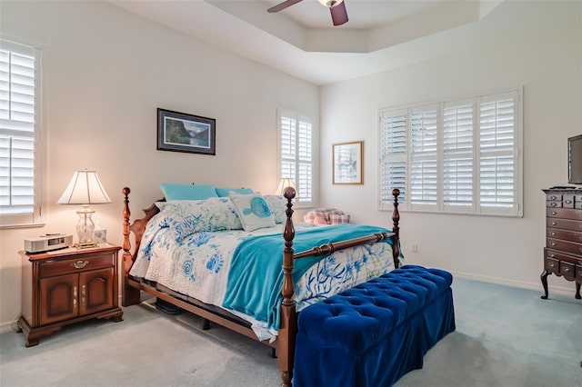 carpeted bedroom with a raised ceiling and ceiling fan